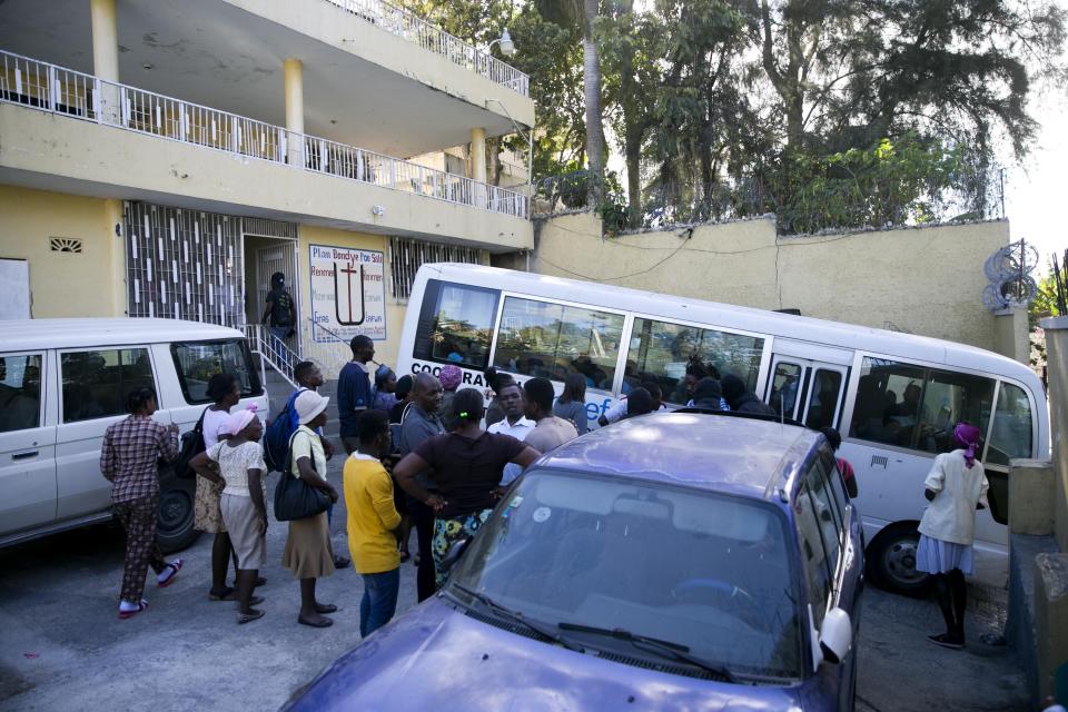 Employees stand outside another branch of the Orphanage of the Church of Bible Understanding, in the Kenscoff area, during a police raid in which all the children were removed and placed on a bus, outside Port-au-Prince, Haiti, Friday, Feb. 14, 2020. A fire swept through a nearby orphanage also run by the Pennsylvania-based nonprofit group, killing 15 children, officials said Friday. (AP Photo/Dieu Nalio Chery)