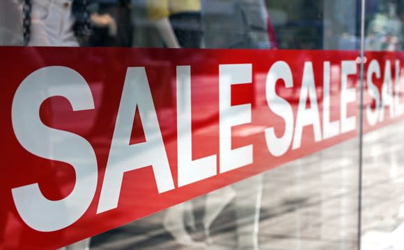 A sale sign in a shop window with mannequins in the background.