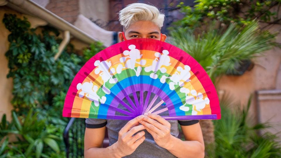 a person holds a rainbow colored disney fan with white images of mickey mouse on it