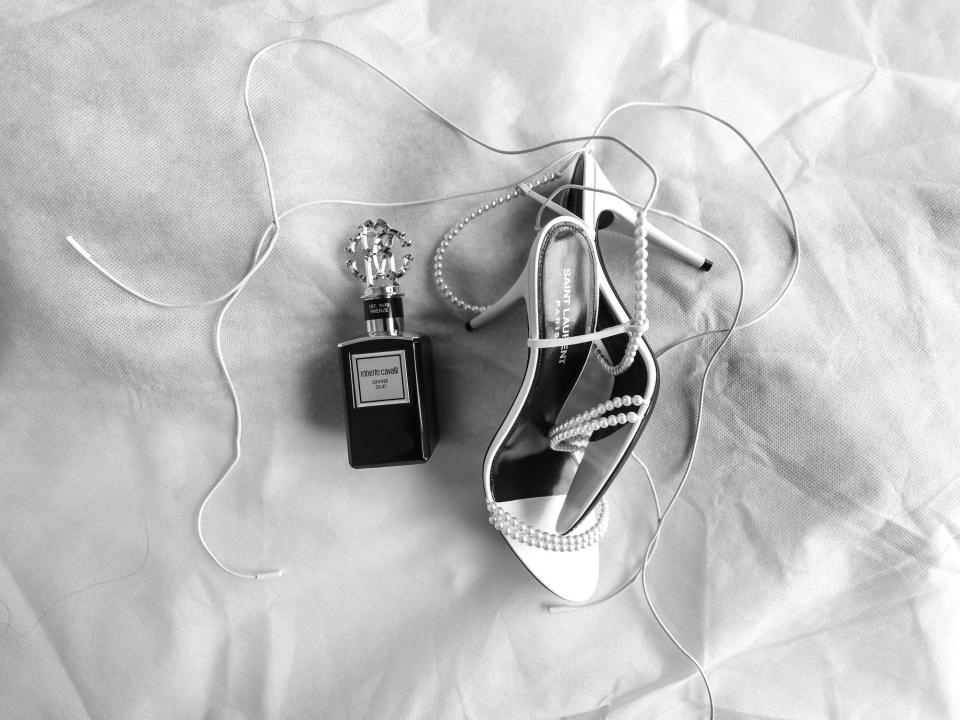 A pair of shoes and a bottle of perfume sit on a bed.