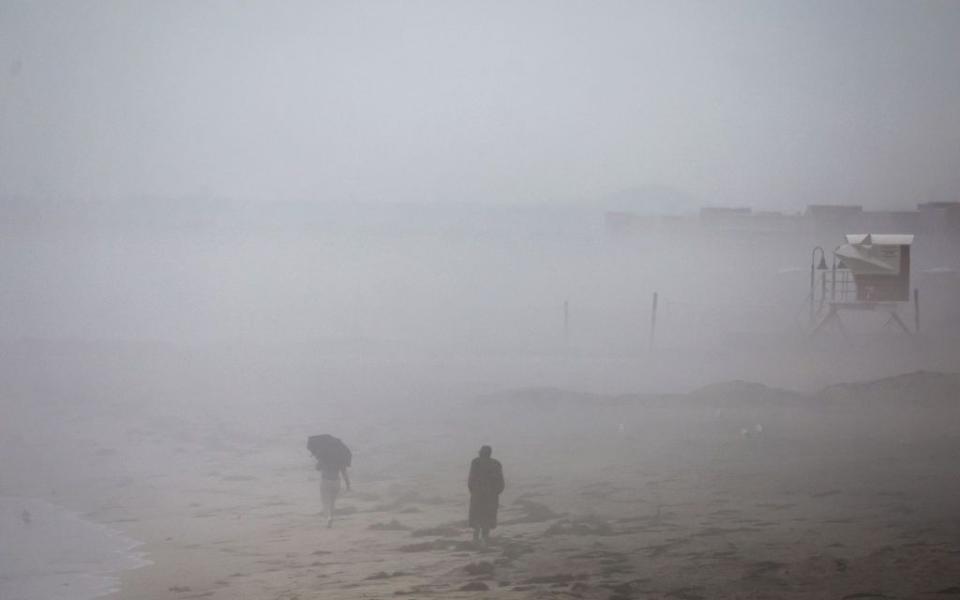 People walk in the rain along the Pacific Ocean with Tropical Storm Hilary approaching San Diego County on Sunday.
