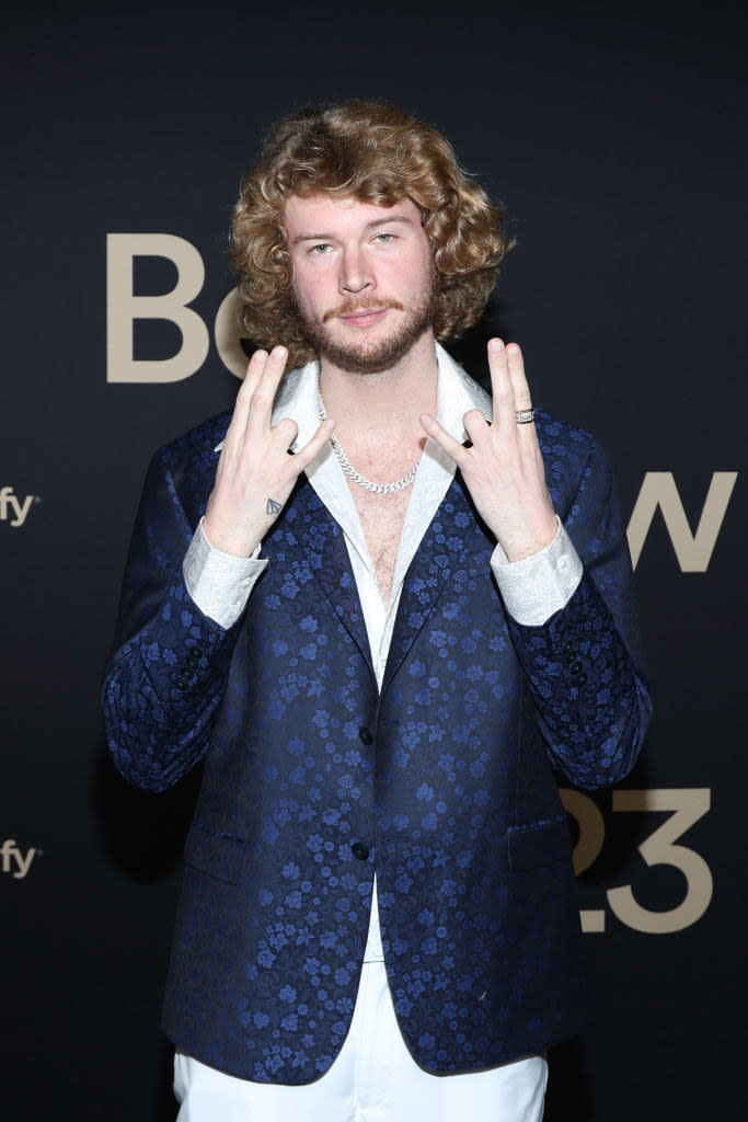 Close-up of Yung Gravy in a suit and holding his hands up