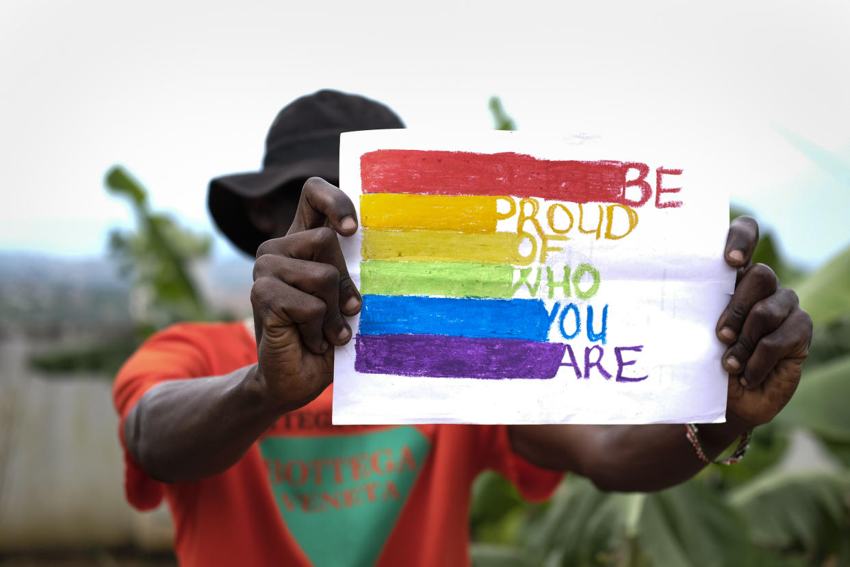 A gay man in Uganda holds a pride sign that reads: Be proud of who you are.