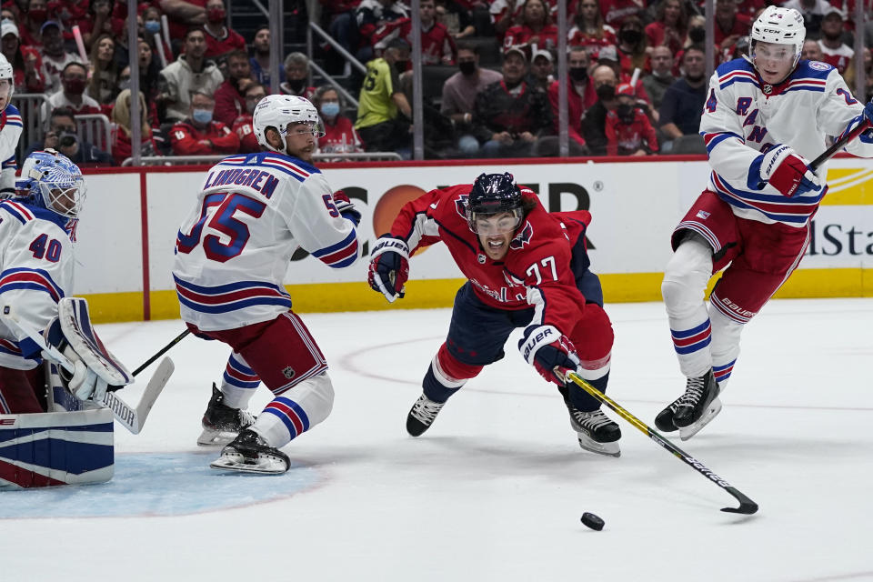 Washington Capitals right wing T.J. Oshie (77) reaches for the puck from between New York Rangers defenseman Ryan Lindgren, left, and right wing Kaapo Kakko (24) during the first period of an NHL hockey game Wednesday, Oct. 13, 2021, in Washington. (AP Photo/Alex Brandon)