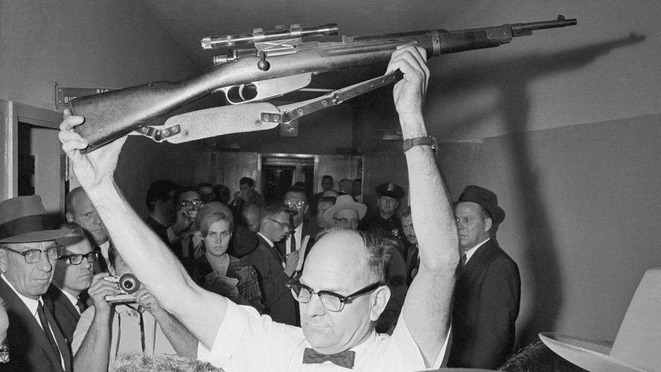 policeman holds a rifle with both hands above his head in a crowded hallway