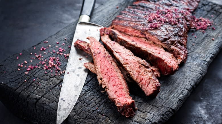 sliced cooked flap steak on a board with a knife