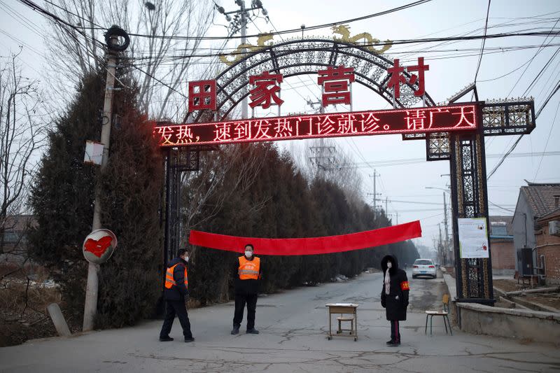 Village committee members wearing face masks and vests stand at the entrance of a community to prevent outsiders from entering, as the country is hit by an outbreak of the new coronavirus, in Tianjiaying village, outskirts of Beijing