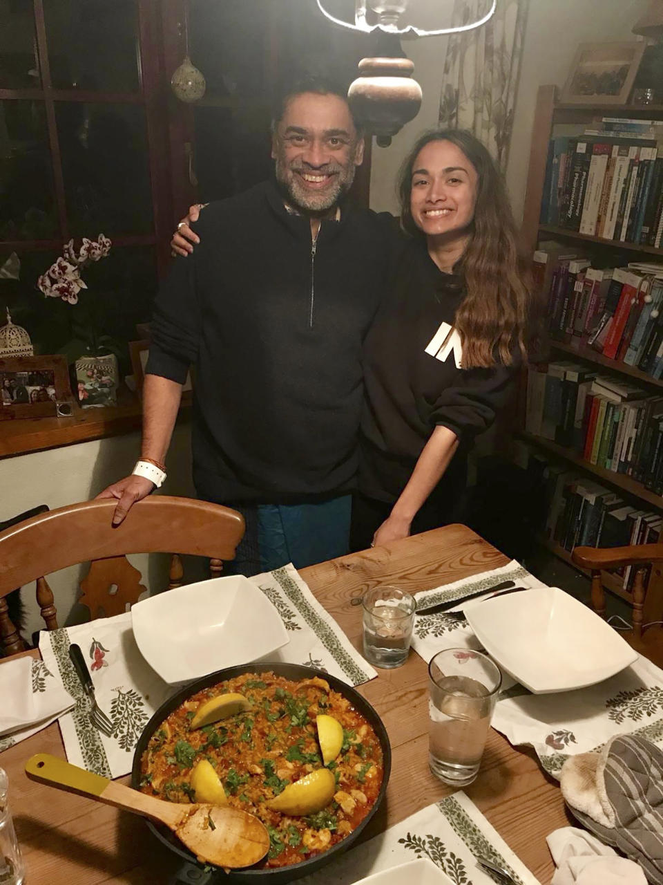 In this image taken on April 9, 2020 Dr. Poorna Gunasekera poses for a photo with his daughter Saki with the 'Paella' dish prepared as his welcome home dinner in the village of Filham, Devon, England after returning from hospital. At his darkest moment in his struggle with the coronavirus, Dr. Poorna Gunasekera glimpsed the first rays of light when three of his former students came to help. Having endured a severe deterioration in his COVID-19 symptoms after around 12 days of contracting the virus, Gunasekera was rushed to Derriford Hospital in Plymouth, in the early hours of March 30. "It was wonderful that during that time, two of my former students, who are doctors, and another who was a nurse, actually came and they identified themselves," he told The Associated Press over several interviews following his release from hospital on April 9. (George Petrie via AP)