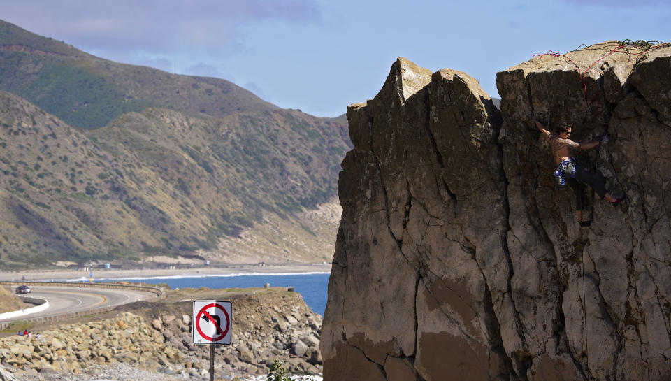 A climber climbs a rock formation along the Pacific Coast Highway, Monday, March 23, 2020, in Malibu, Calif. Officials are trying to dissuade people from using the beaches after California Gov. Gavin Newsom ordered the state's 40 million residents to stay at home indefinitely. His order restricts non-essential movements to control the spread of the coronavirus that threatens to overwhelm the state's medical system. (AP Photo/Mark J. Terrill)