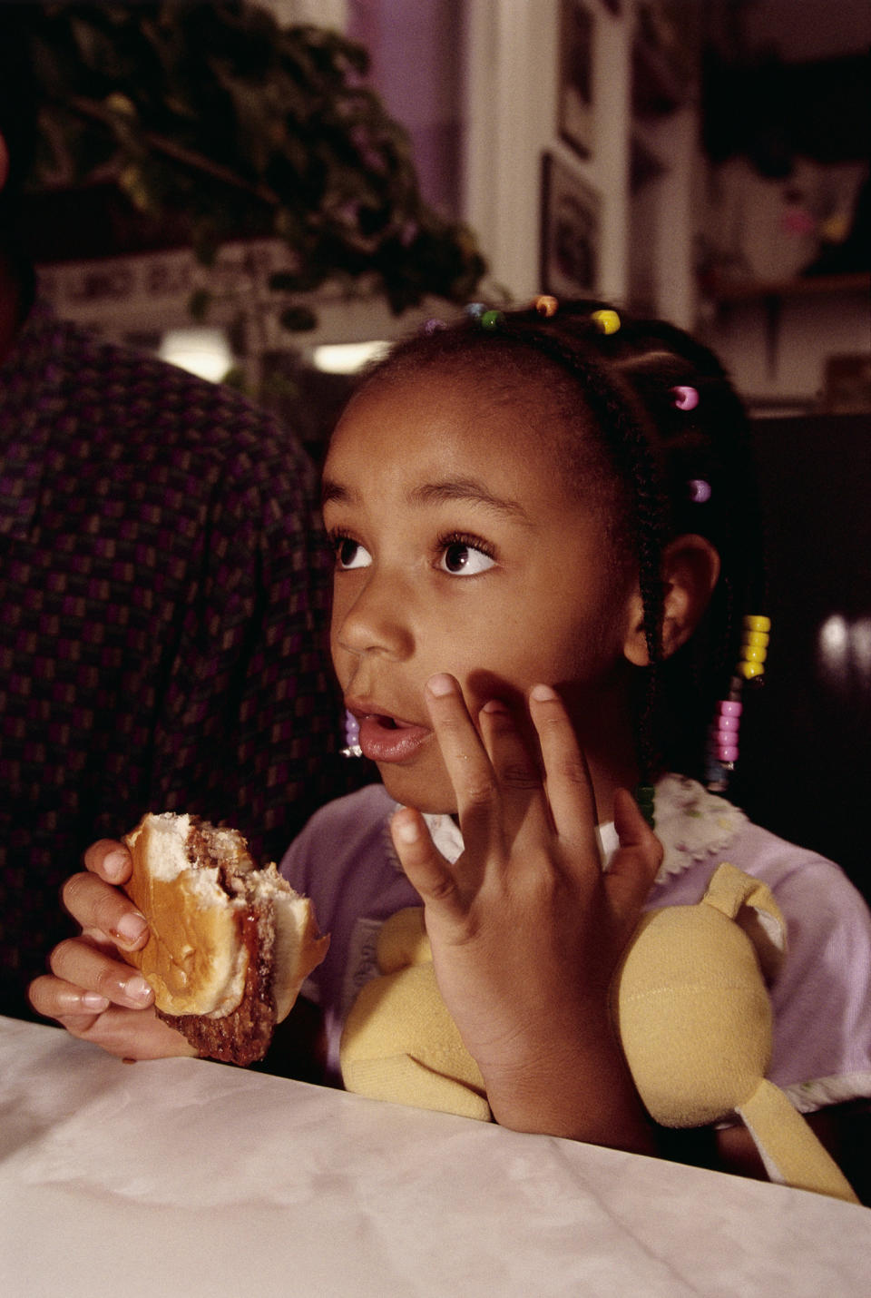 Young girl eating a sandwich, looking thoughtful, sitting indoors