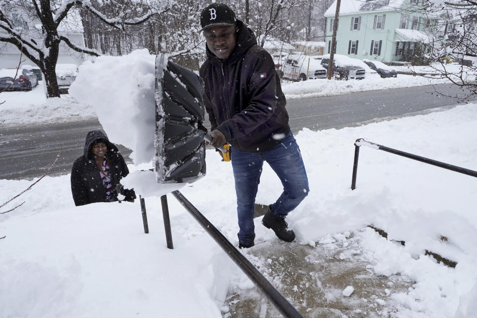 Berry Greg, of Leominster, Mass., front, shovels snow off the front steps of his home while his wife Myrianna Jean Pierre, behind left, looks on, Tuesday, March 14, 2023, in Leominster. The New England states and parts of New York are bracing for a winter storm due to last into Wednesday. (AP Photo/Steven Senne)