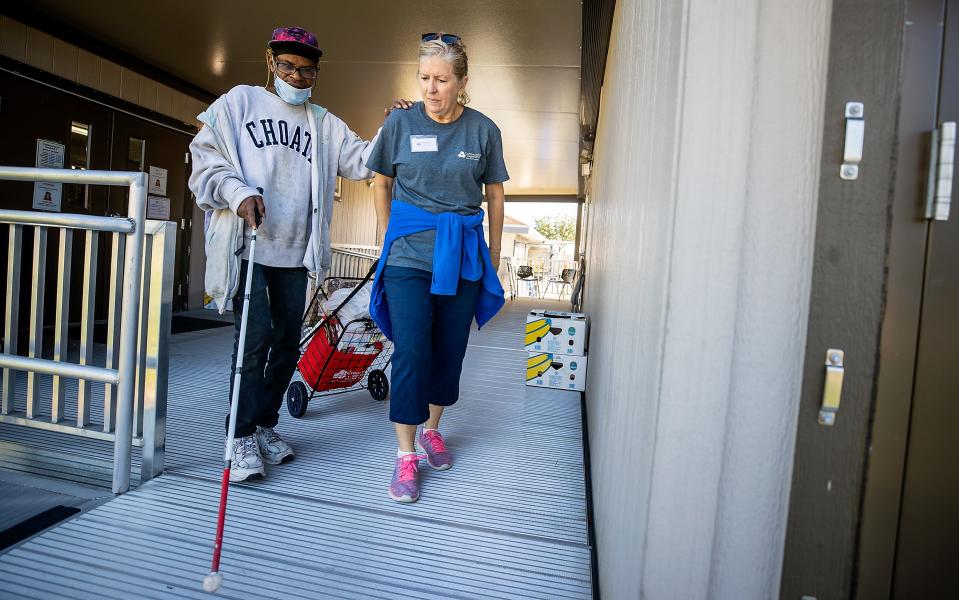 Deb Nelson, a volunteer at the Community Cooperative in Fort Myers, helps Anthony Armstrong make his way home after shopping in the Cooperative's community market in Fort Myers recently.