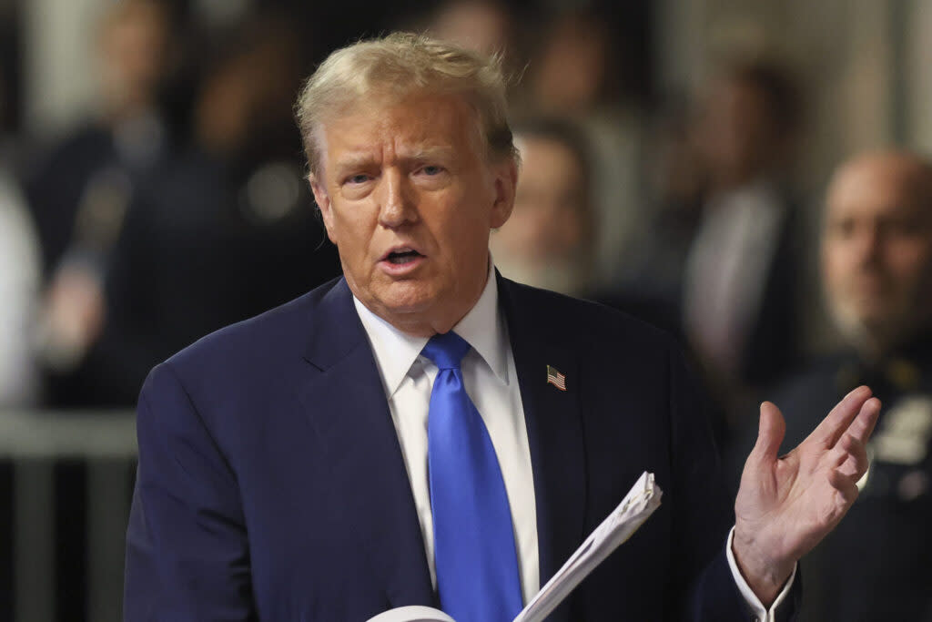 A man in a dark blue suit and blue tie gesturing