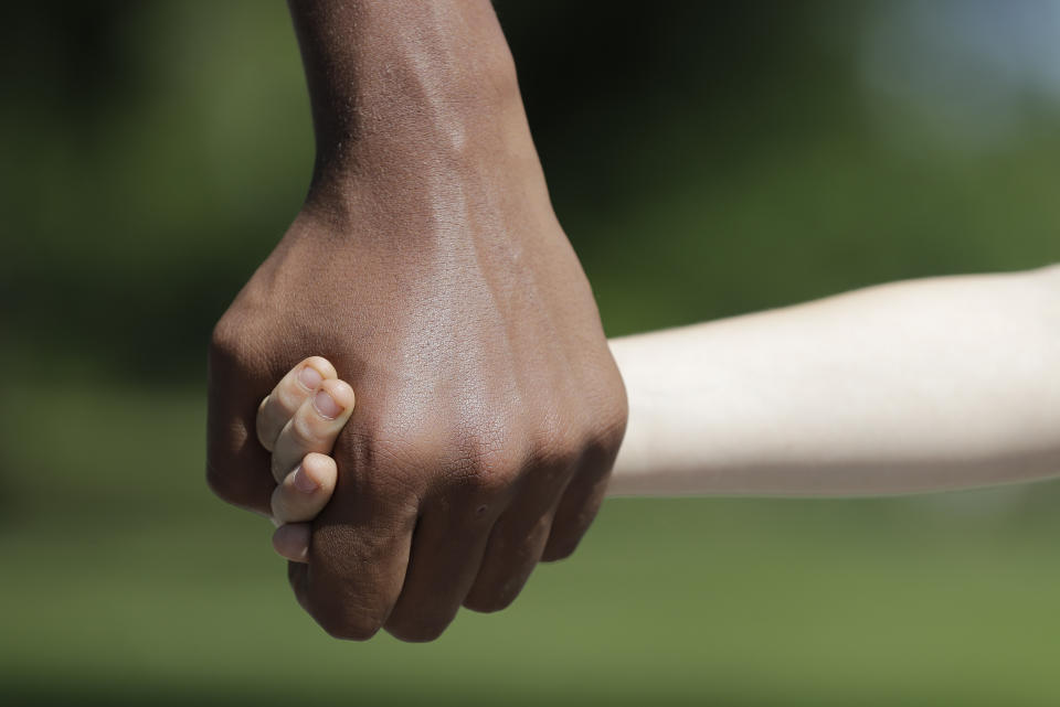 Belachew Neal holds hands with his younger brother, Elisha, at Garfield Park, Sunday, June 14, 2020, in Indianapolis. The Associated Press discussed race with six white couples who have adopted or have custody of Black children. These parents are trying to help their children understand race in America while getting an accelerated course themselves. (AP Photo/Darron Cummings)