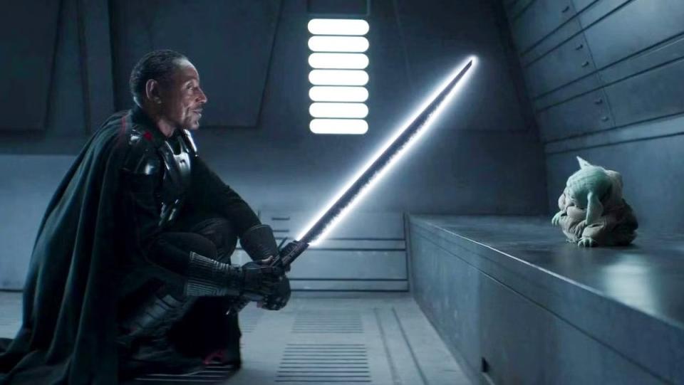Moff Gideon kneels with the Darksaber before him in a cell oppoite Grogu lying on a bench on The Mandalorian