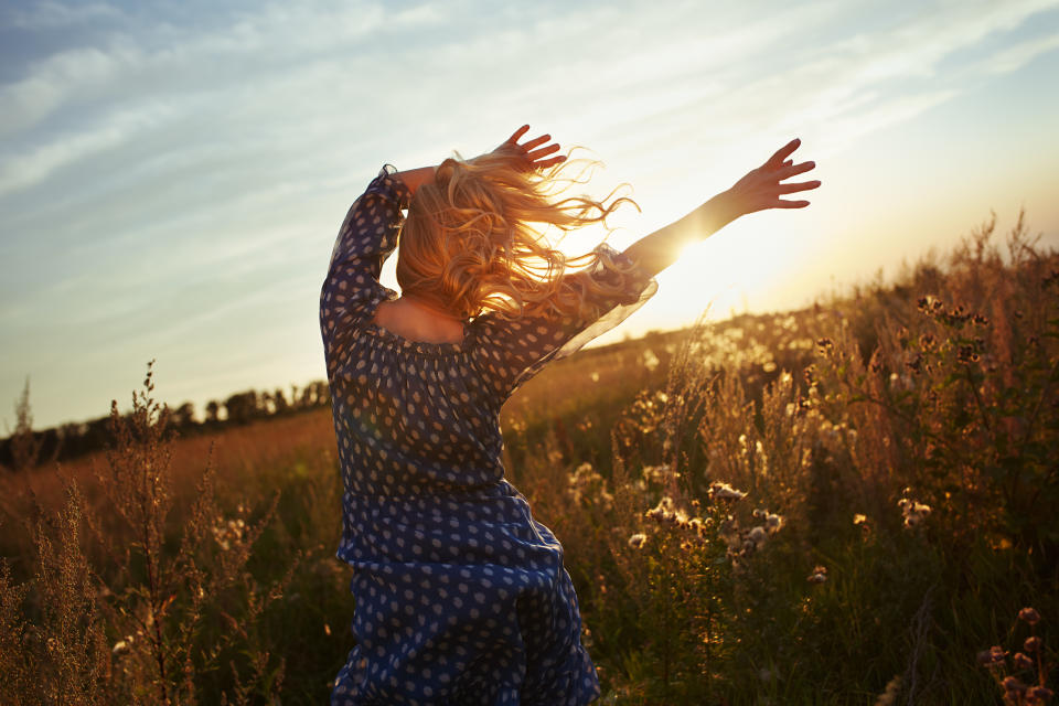 Woman with wavy hair dancing in the meadow during sunset