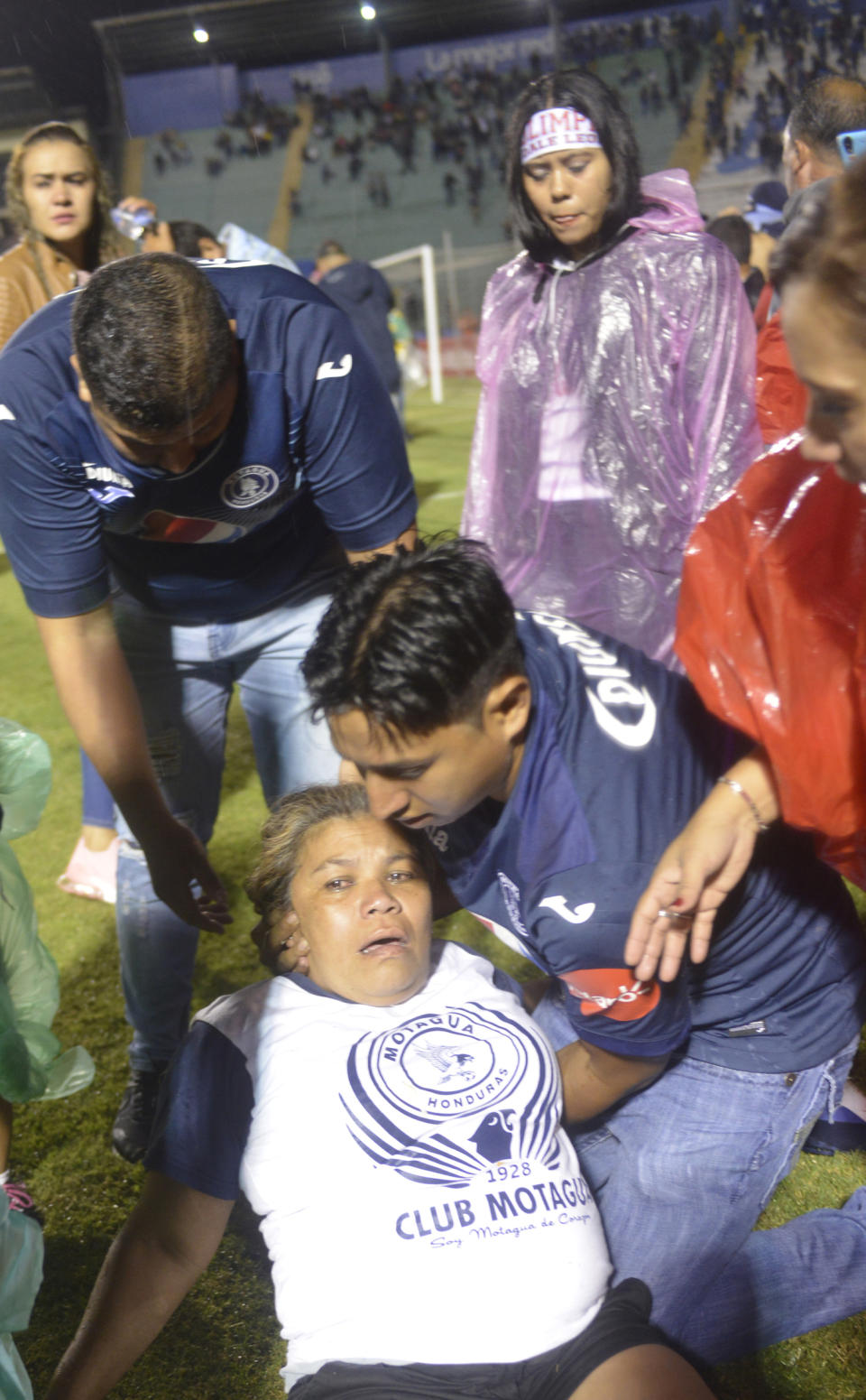 A soccer fan affected by tear gas fired by police is helped on the field by fellow fans after a deadly fight broke out before the start of a game between Motagua and Olimpia, inside the national stadium in Tegucigalpa, Honduras, late Saturday, Aug. 17, 2019. The fight between fans of rival soccer teams outside the stadium left three people dead and led to the suspension of the game. (Victor Colindres/La Tribunal via AP)