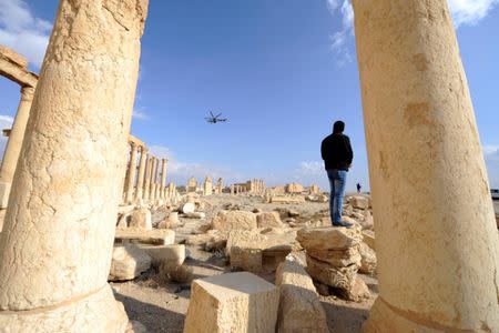 A man looks towards a Russian helicopter as it flies over ruins in the historic city of Palmyra, Syria March 4, 2017. REUTERS/Omar Sanadiki