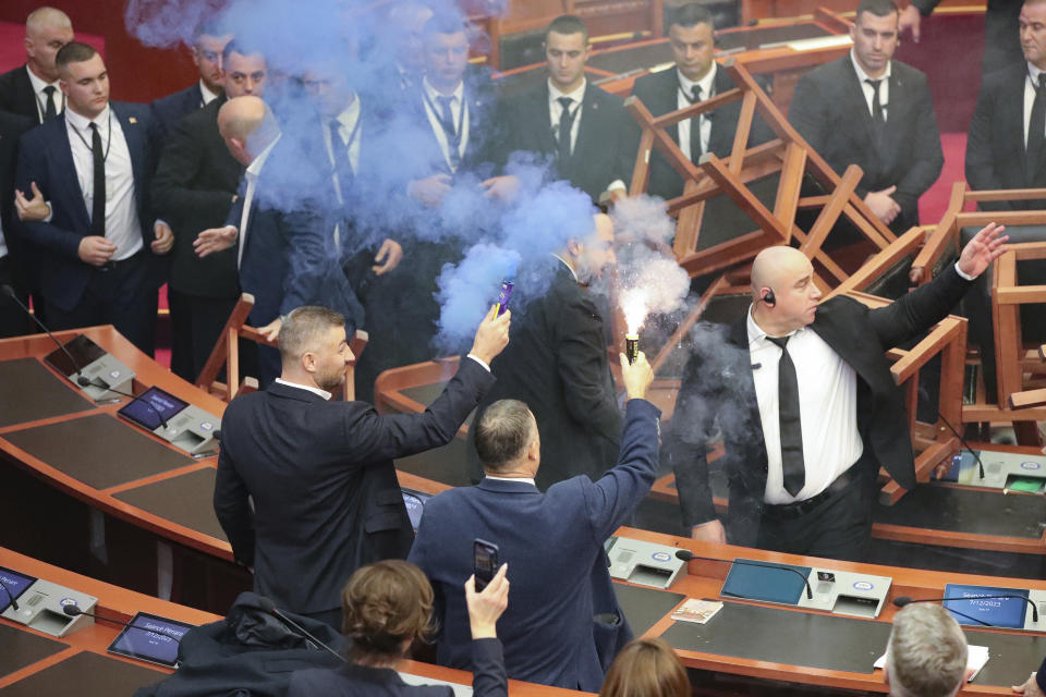 Bledion Nallbati, left and Asllan Gogjani, Democratic lawmakers, hold flares during a parliament session in Tirana, Albania, Thursday Dec. 7, 2023. The Albanian Parliament on Thursday passed the annual budget and other draft laws in a disrupted vote from the opposition using flares and noise to protest against what they consider as an authoritarian rule from the governing Socialist Party. (AP Photo/Armando Babani)