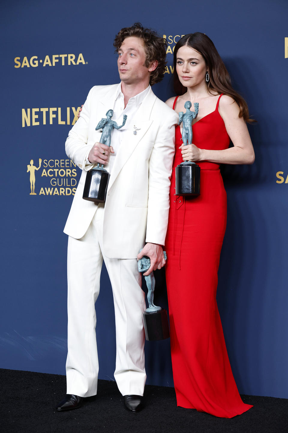 Jeremy Allen White in a white suit and Ayo Edebiri in a red dress, holding Screen Actors Guild Awards at the SAG-AFTRA event backdrop