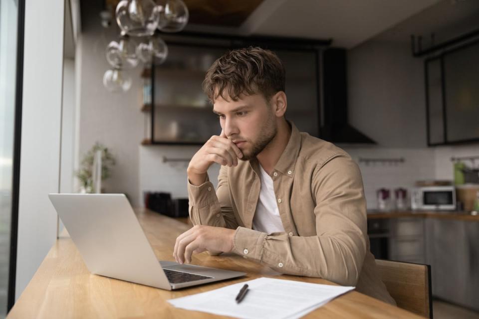 A person sitting at a table with a laptop, piece of paper, and writing utensil.