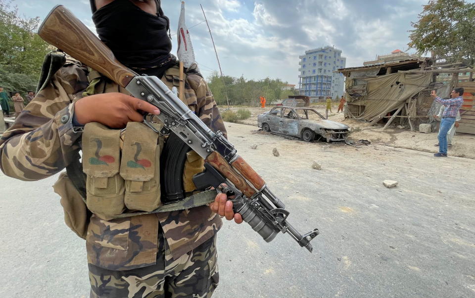 A member of Taliban forces stands guard as Afghan men take pictures of a vehicle from which rockets were fired, in Kabul on Monday.