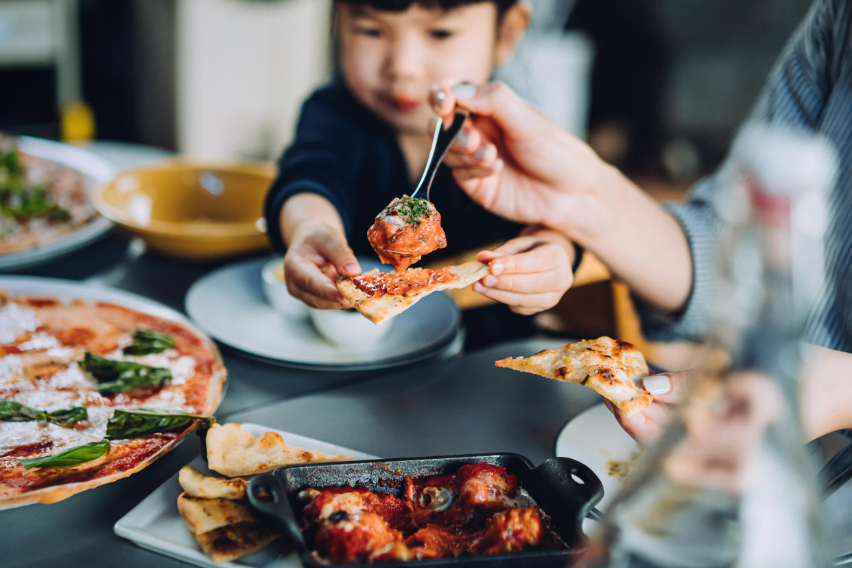 Close up of young Asian mother and lovely little daughter enjoying pizza lunch in an outdoor restaurant while mother serving meatballs and bolognese to daughter. Family enjoying bonding time and a happy meal together. Family and eating out lifestyle