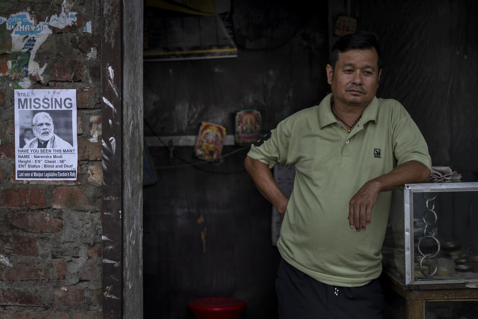 A shopkeeper stands next to a poster criticising the silence from Prime Minister Narendra Modi following ethnic clashes and rioting, in Imphal, capital of the northeastern Indian state of Manipur, Thursday, June 22, 2023. Manipur is caught in a deadly conflict between two ethnic communities that have armed themselves and launched brutal attacks against one another, killing at least 120. The unrest has been met with nearly two months of silence from Prime Minister Narendra Modi, whose Bharatiya Janata Party rules Manipur. (AP Photo/Altaf Qadri)