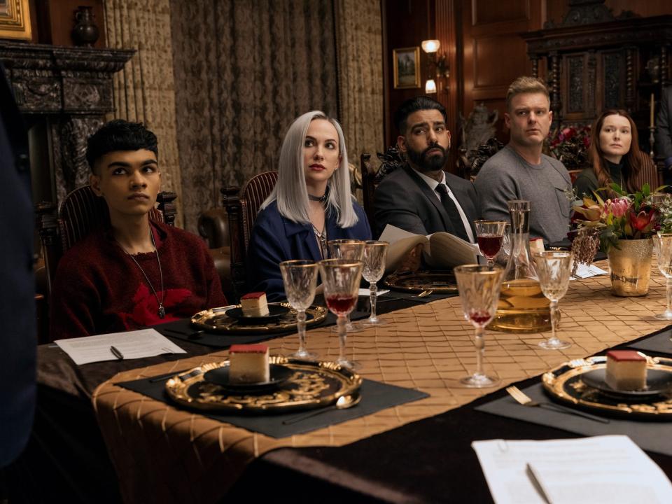 The cast of Netflix's "The Fall of the House of Usher." Each person is dressed differently, from casual to business clothes, and is sitting at a fancy table setting in what appears to be a mansion