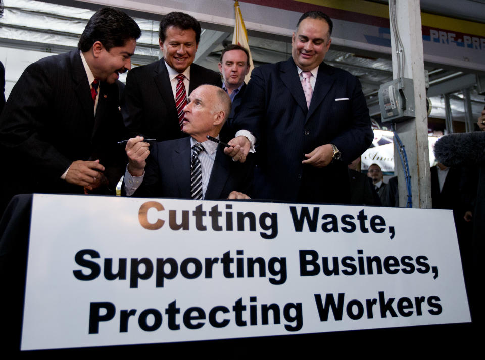 California Gov. Jerry Brown, seated, borrows a pen from California Assembly member Jose Solorio, left, as he signs a bill aimed at worker's compensation costs at a printing company in San Diego. Looking on from right are California Assembly Speaker John Perez, Art Polaski of the California Labor Federation, and California Assembly member Marty Block. Brown signed the bill intended to reduce workers' compensation costs for California businesses while increasing benefits to injured workers. (AP Photo/Gregory Bull)