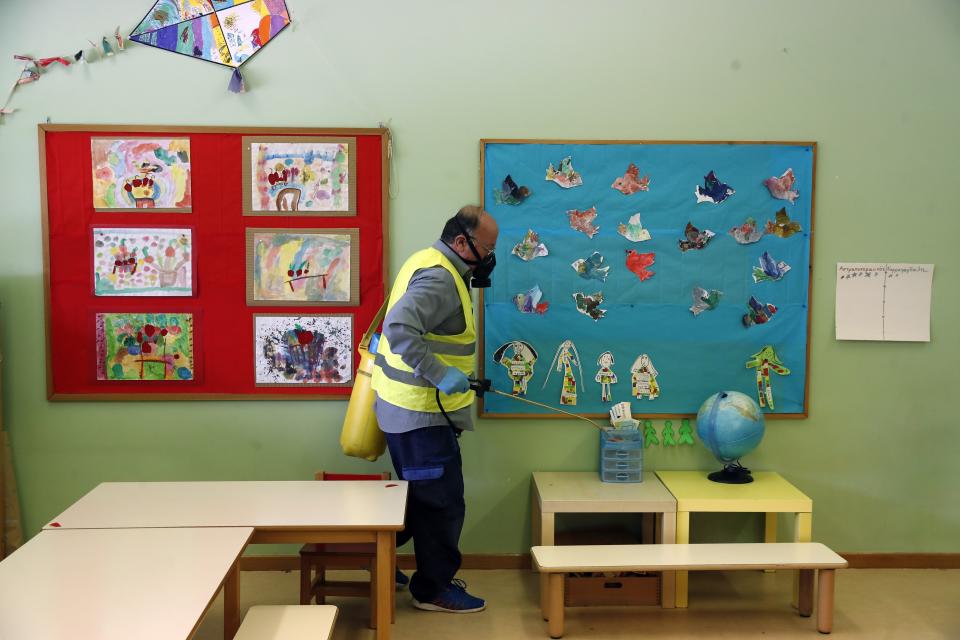 A worker wearing a protective mask sprays disinfectant inside a classroom of a kindergarten in the suburb of Halandri, northern Athens, Friday, May 29, 2020. Greece will reopen preschools, kindergartens and primary schools on Monday in the latest round of easing coronavirus pandemic restrictions imposed in late March. Classes will have no more than 15 children while the academic year will end on Friday, June 26. (AP Photo/Thanassis Stavrakis)