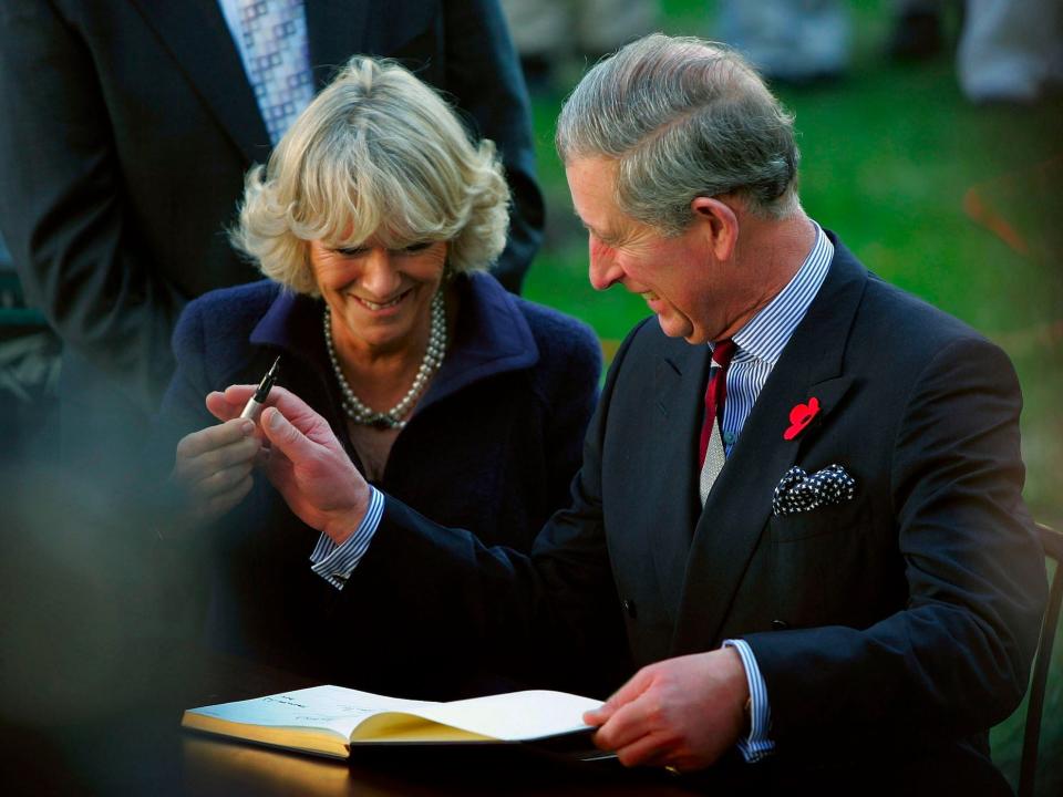 Camilla, Queen Consort and King Charles III laugh as he passes a pen to her.