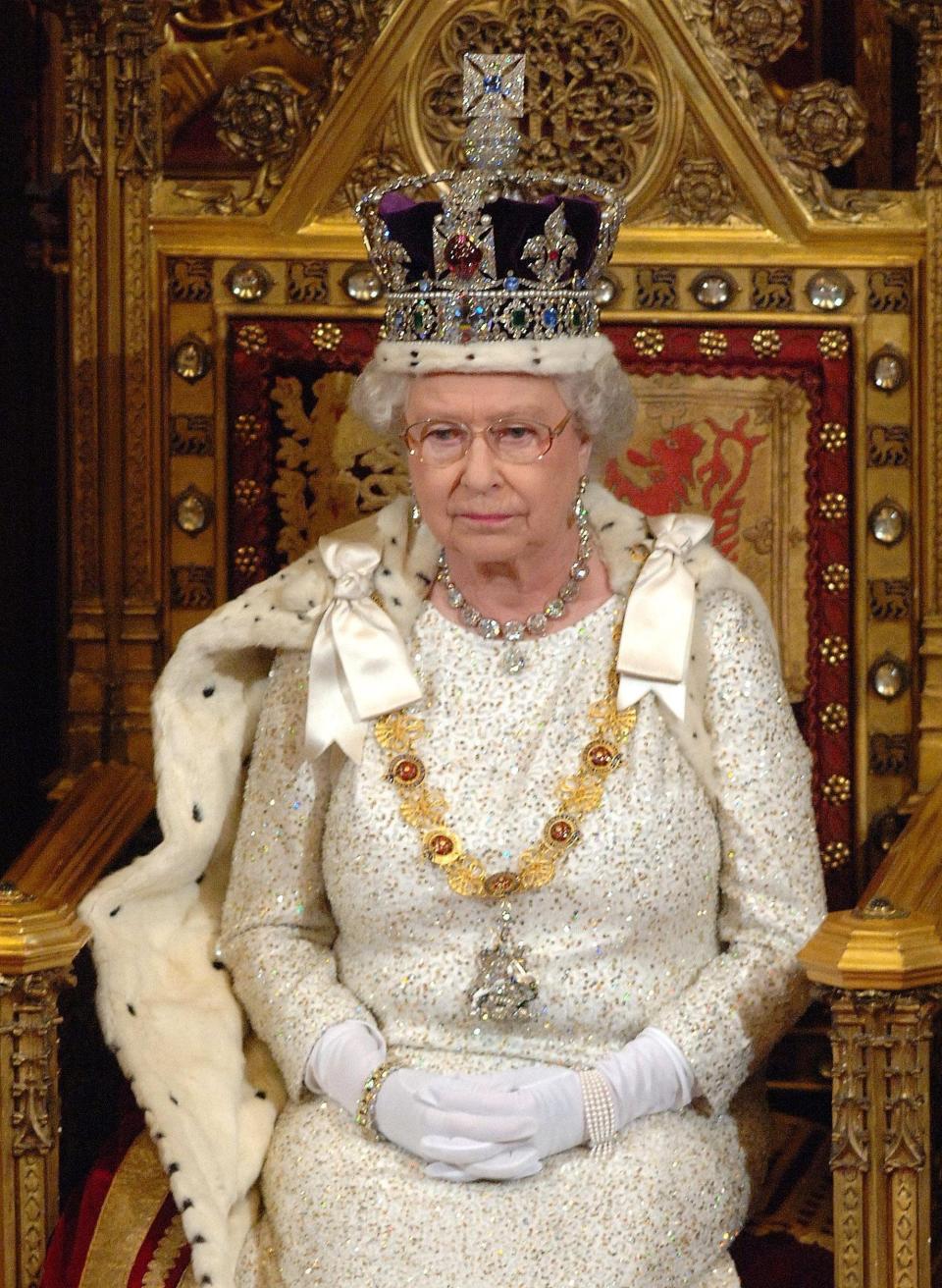 Queen Elizabeth wears the Imperial State Crown as she sits on a throne.