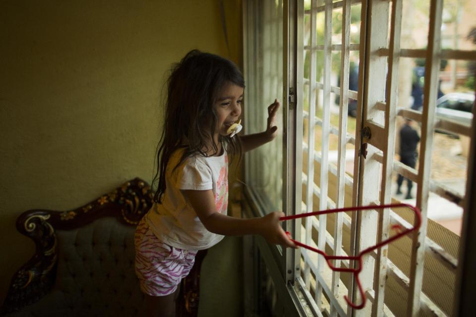 EDS NOTE - SPANISH LAW REQUIRES THAT THE FACES OF MINORS ARE MASKED IN PUBLICATIONS WITHIN SPAIN - Police stand guard blocking the apartment's entrance as Fernando Montoya Jimenez's grandchild looks through the window during Fernando's eviction in Madrid, Spain, Wednesday, July 23, 2014. Fernando Montoya Jimenez, 61, lived with his son Jesus Miguel, 14, and his 16-year old daughter Diana, who is six months pregnant, in an apartment owned by the Madrid Community state housing company for more than 20 years, paying subsidized rent. Jimenez, who has a disability and epilepsy and has spent time in prison for prior convictions, lives from a state benefit of euro 311 (US$419) per month. The state housing company evicted him and his family after freezing his account with them when he failed to pay his rent. (AP Photo/Andres Kudacki)