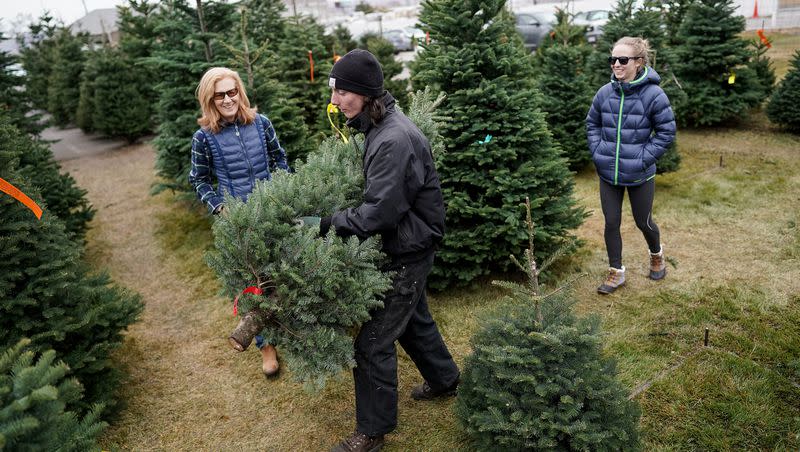 Justice Van Horne carries a Christmas tree for Linda Karz, left, and her daughter Jessica after they picked it out at a Robinson Tree Farms lot in South Salt Lake on Dec. 13, 2019.