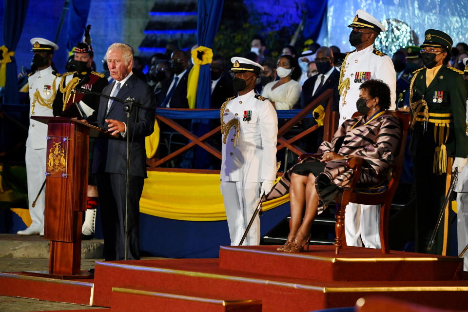 Prince Charles at the microphone, watched by President Sandra Mason and officials in white military uniforms.