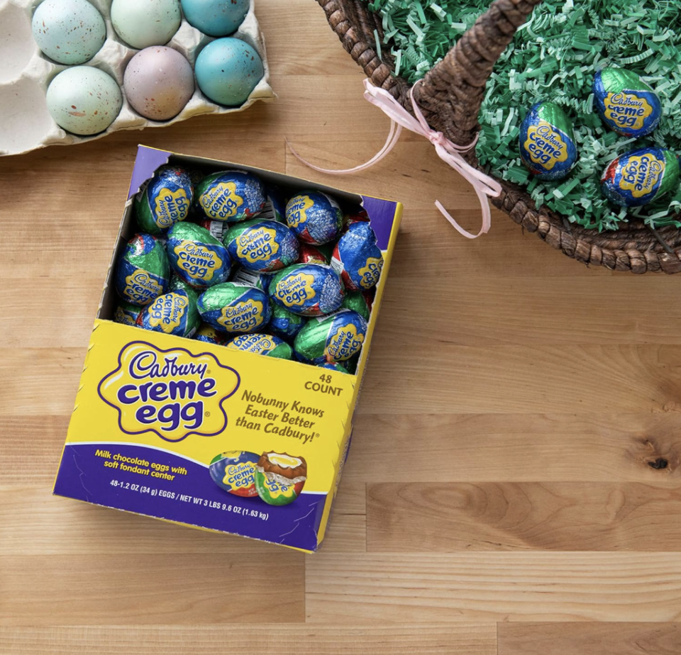 a box of cadbury creme eggs on a wooden table next to dyed eggs and an Easter basket