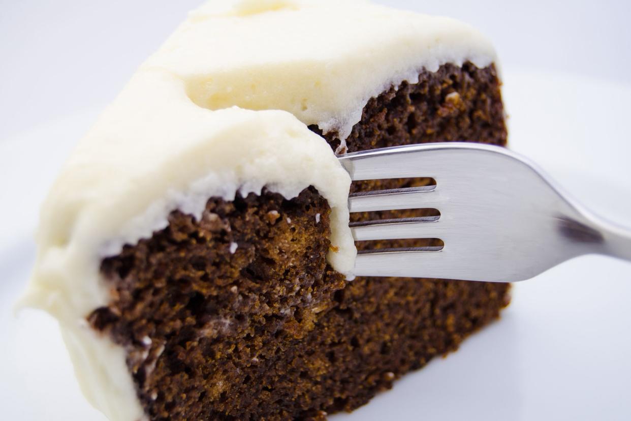 Closeup of fork cutting through a piece of sugarless spice cake on a white plate with a white background