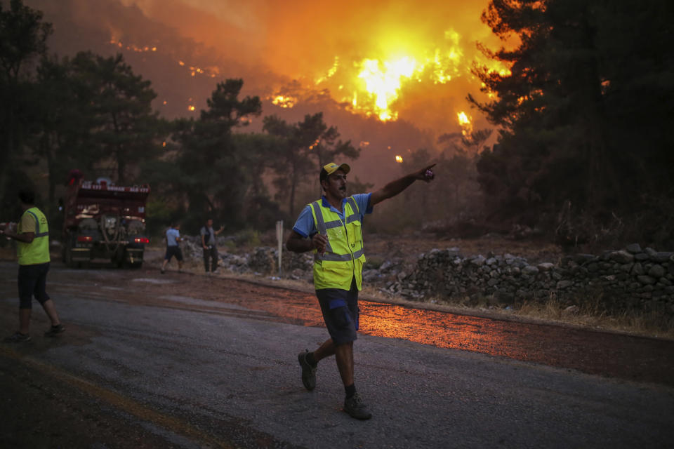 A firefighter points walking away from an advancing fire that rages Cokertme village, near Bodrum, Turkey, Monday, Aug. 2, 2021. For the sixth straight day, Turkish firefighters battled Monday to control the blazes that are tearing through forests near Turkey's beach destinations. Fed by strong winds and scorching temperatures, the fires that began Wednesday have left eight people dead. Residents and tourists have fled vacation resorts in flotillas of small boats or convoys of cars and trucks. (AP Photo/Emre Tazegul)