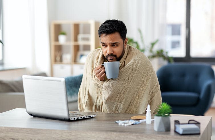 A man with a cold, wrapped in a blanket, working on his laptop