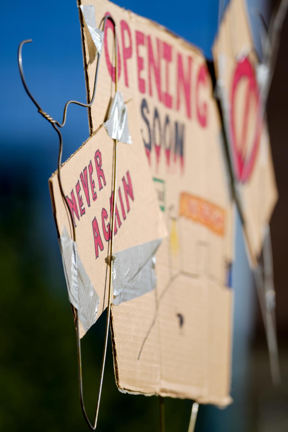 A detailed shot of a 'Never Again' sign attached to a hanger sign during the rally and march for abortion rights Wednesday, May 4, 2022, at Red Arrow Park in downtown Milwaukee. If the 1973 decision is over turned, a 19th century state law would back Wisconsin doctors from performing abortions except when saving the life of the mother.