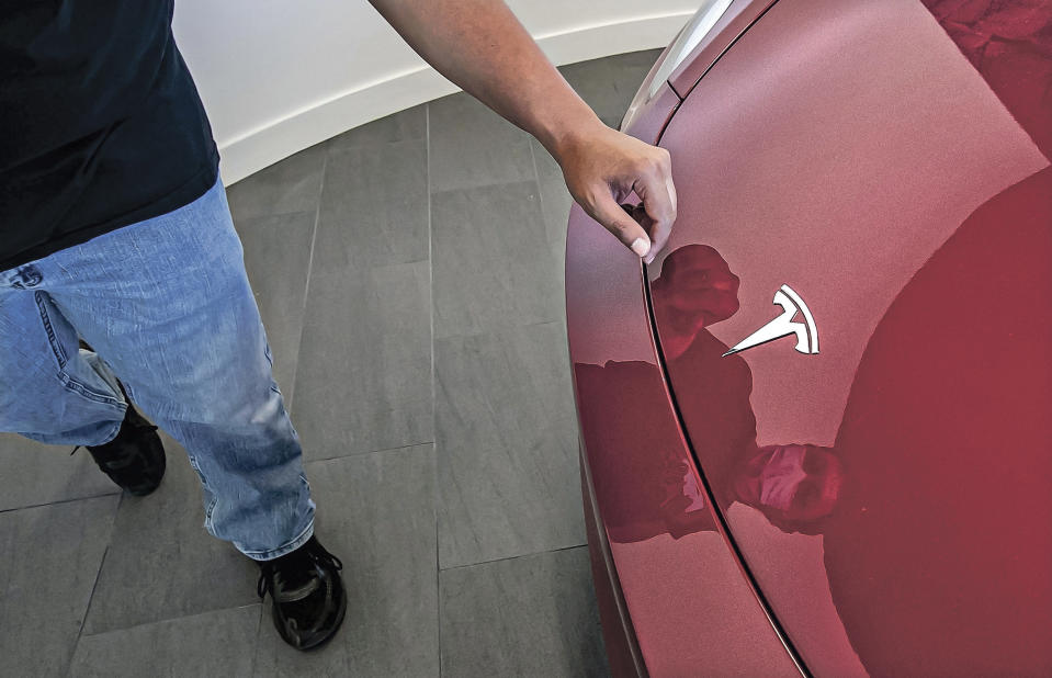 In this Sept. 9, 2021 photo, Dietrich Ginocchio rubs a smudge off the Tesla emblem on a Tesla Y model during an event to celebrate a partnership between Tesla and the Nambé Pueblo after the electric car company repurposed a defunct casino into a sales, service and delivery center near Santa Fe, N.M. Tesla has opened a store on tribal land in New Mexico, sidestepping car dealership laws that prohibit car companies from selling directly to customers. (Jim Weber/Santa Fe New Mexican via AP)