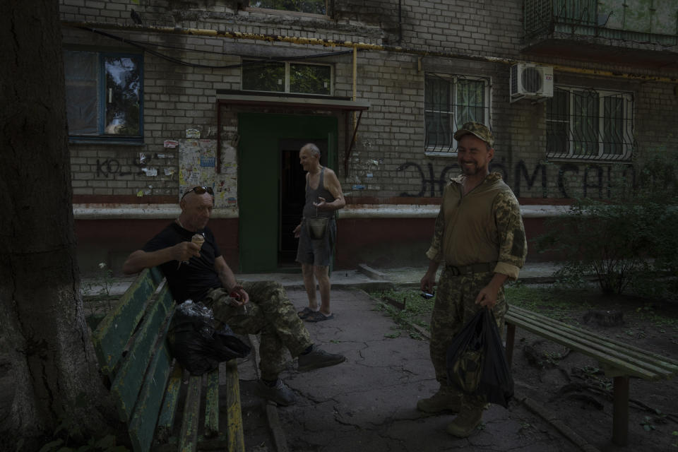 Soldiers rest and eat ice-cream on benches in front of the apartment building Seventy-year-old pensioner Valerii Ilchenko, who lives alone and is refusing to evacuate, in Kramatorsk, eastern Ukraine, Wednesday, July 6, 2022. Ilchenko, a former soldier in the Soviet army, is furious at the Russians. He wants them to be "expelled as soon as possible" and sent back to their towns. (AP Photo/Nariman El-Mofty)
