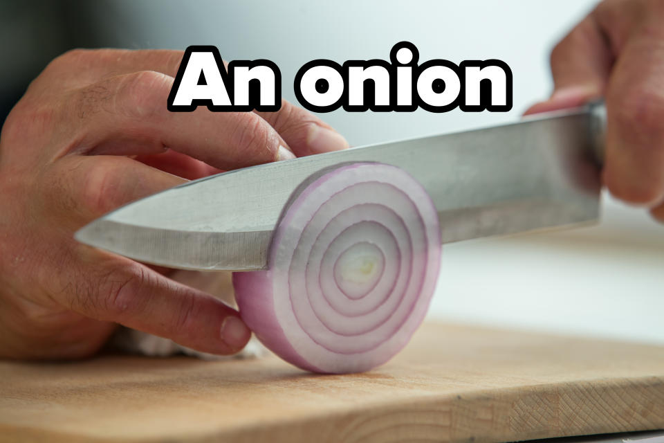 Close-up of a person thinly slicing a red onion on a wooden cutting board with a sharp knife