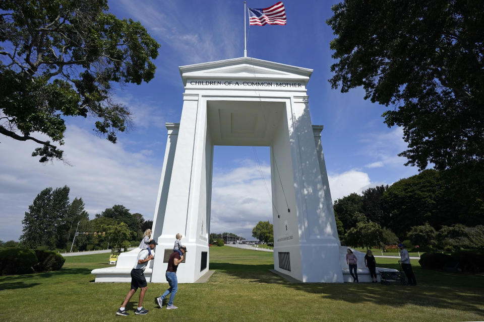 People walk adjacent to the border with Canada at the Peace Arch in Peace Arch Historical State Park, where cars behind wait to enter Canada at the border crossing Monday, Aug. 9, 2021, in Blaine, Wash. Canada lifted its prohibition on Americans crossing the border to shop, vacation or visit, but America kept similar restrictions in place, part of a bumpy return to normalcy from coronavirus travel bans. (AP Photo/Elaine Thompson)