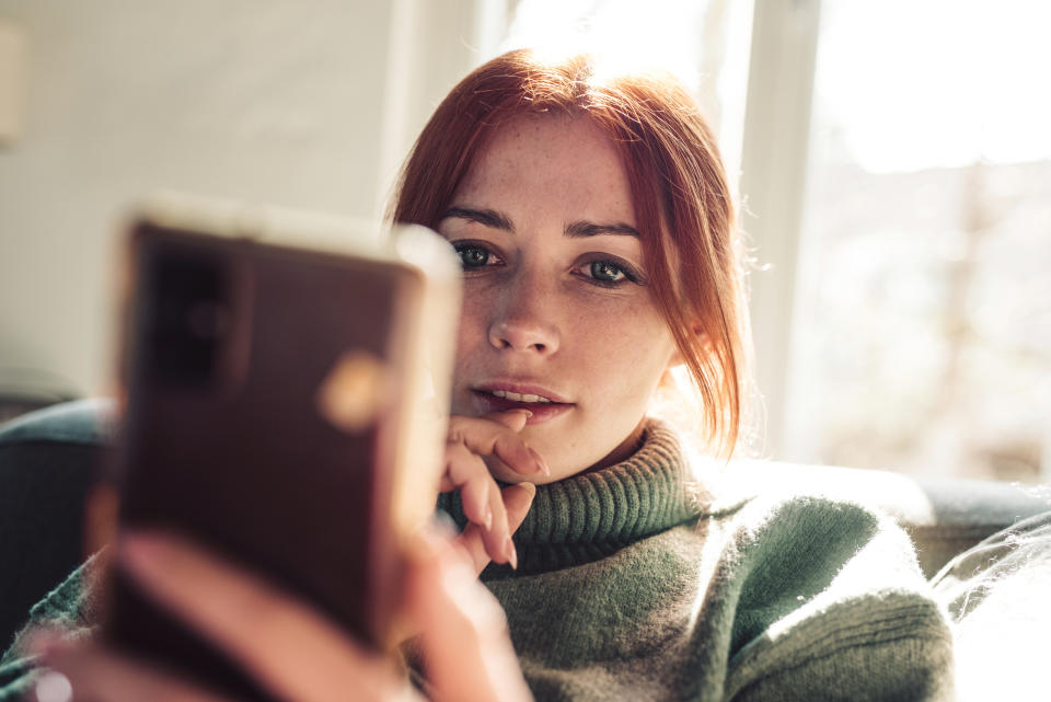 Woman with red hair taking a self-portrait with her phone. She's wearing a turtleneck sweater