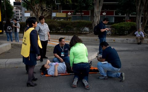 A woman is helped outside, along Reforma Avenue after a 7.2-magnitude earthquake shook Mexico City - Credit: AP Photo/Eduardo Verdugo