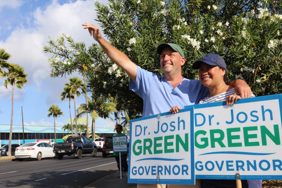 Hawaii Lt. Gov. Josh Green, left, and his wife, Jamie, greet passing cars while campaigning in Honolulu on Aug. 2, 2022. The candidates running in Hawaii's primary election to succeed term-limited Democratic Gov. David Ige include a former first lady, a retired mixed martial arts champion and a congressman who moonlights as a Hawaiian Airlines pilot. (AP Photo/Audrey McAvoy)