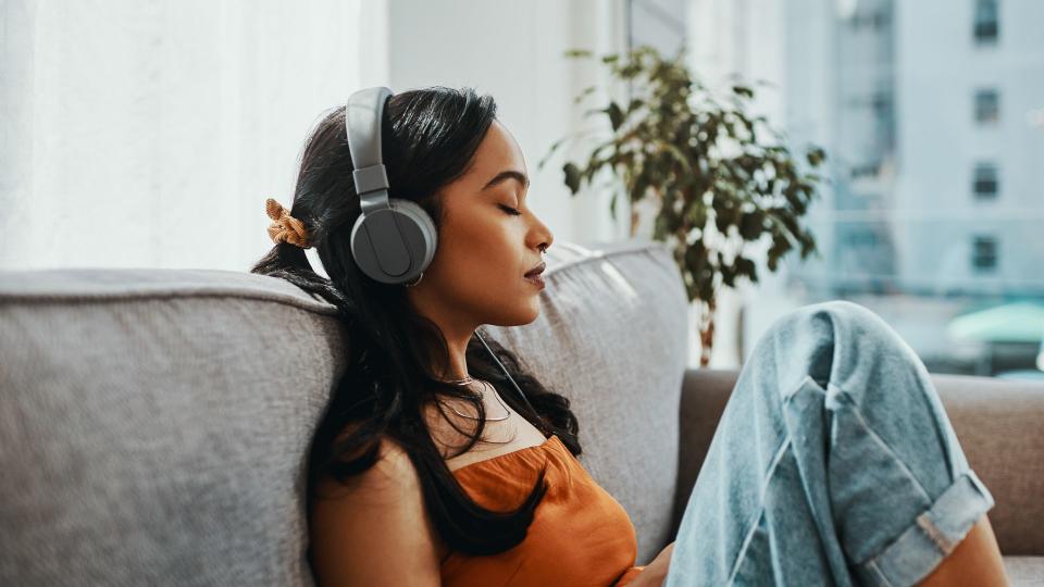 Shot of a young woman using headphones while relaxing on the sofa at home.