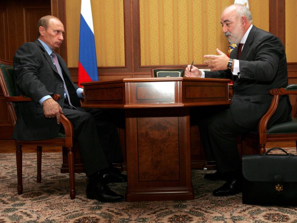 vladimir putin viktor vekselberg sit across table with russian flag in background